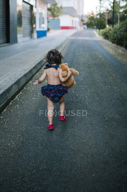 Игривая девочка с плюшевым мишкой бегает по дороге — стоковое фото
