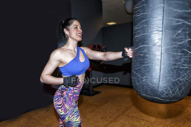 Bella donna sorridente che si allena con il sacco da boxe in palestra — Foto stock