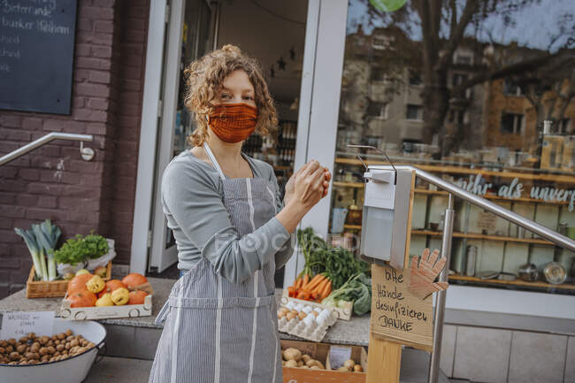 Женщина-клерк протирает руки дезинфицирующим средством, стоя у магазина — стоковое фото
