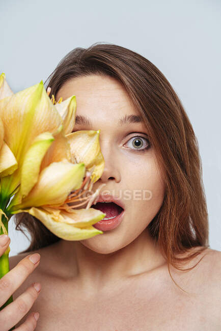 Femme surprise tenant fleur tout en se tenant debout sur fond blanc — Photo de stock