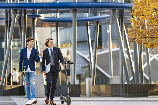 Männliche Profis mit Schieberoller reden beim Gehen auf Gehweg — Stockfoto