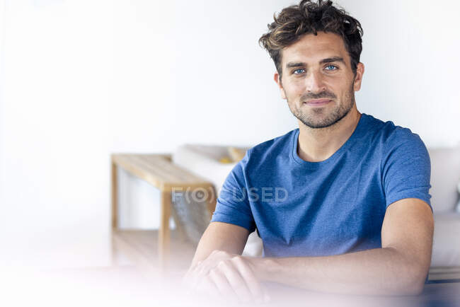 Bello uomo con gli occhi azzurri sorridente mentre seduto a casa — Foto stock