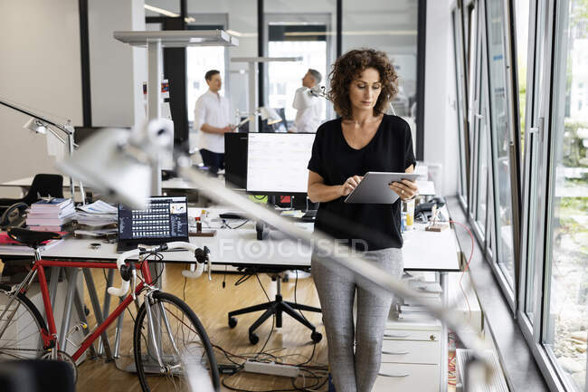Жіночий підприємець працює на цифровій планшеті, стоячи з колегою у відкритому офісі. — стокове фото