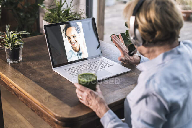Nonna che saluta la nipote in videochiamata attraverso il computer portatile mentre ha succo a casa — Foto stock