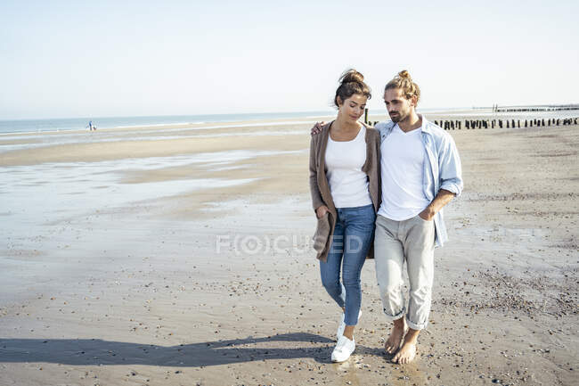 Young couple with hands in pockets taking walk on beach during sunny day — Stock Photo