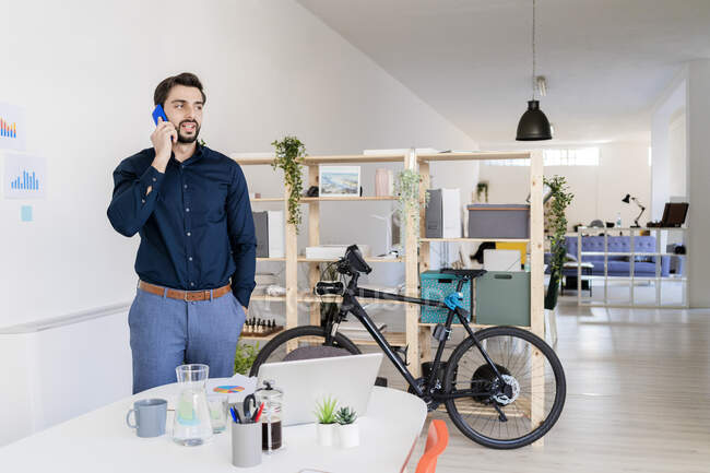 Männlicher Unternehmer telefoniert am Schreibtisch mit der Hand in der Tasche — Stockfoto