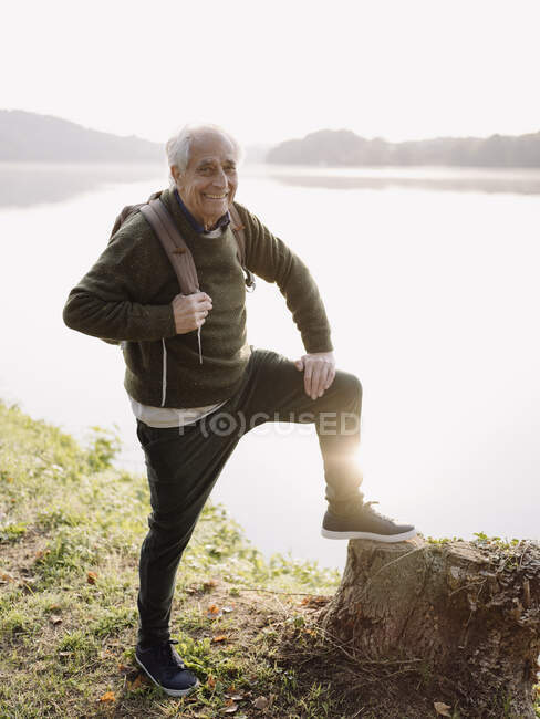Smiling man carrying backpack while standing against lake — Stock Photo