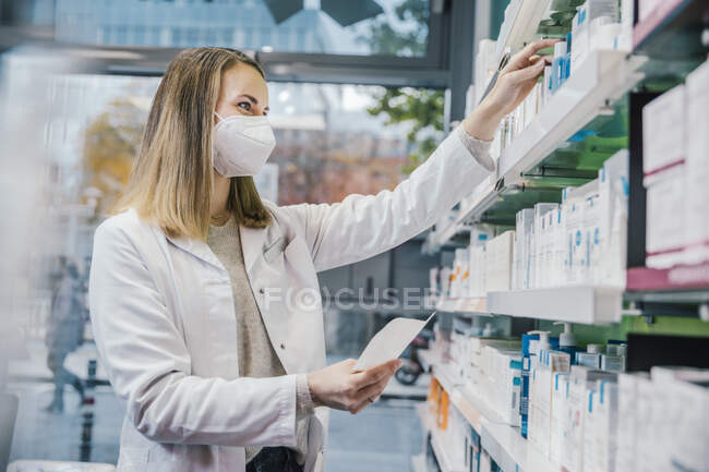 Pharmacienne portant un masque protecteur pendant qu'elle travaillait dans une pharmacie — Photo de stock