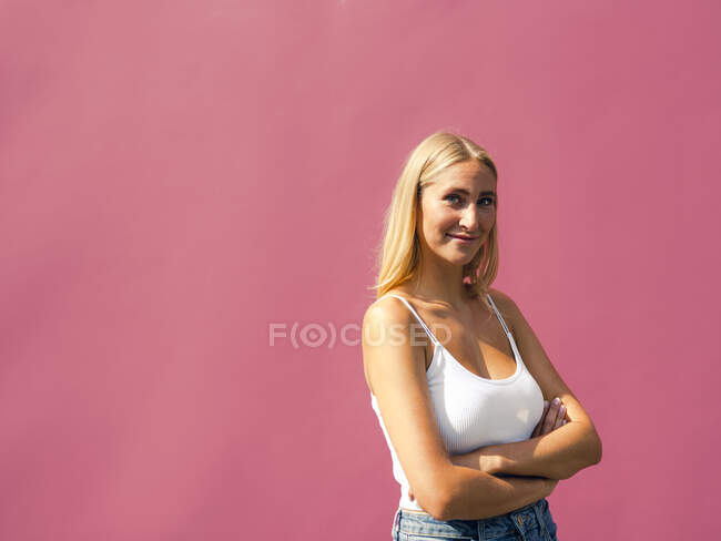 Smiling beautiful woman with arms crossed against pink wall — Stock Photo