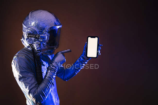 Astronauta en traje espacial apuntando al teléfono inteligente contra el fondo de color - foto de stock