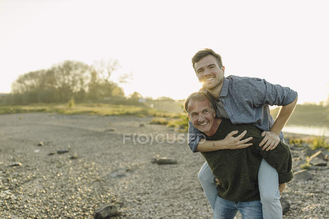 Smiling father giving piggyback ride to son against clear sky at evening — Stock Photo