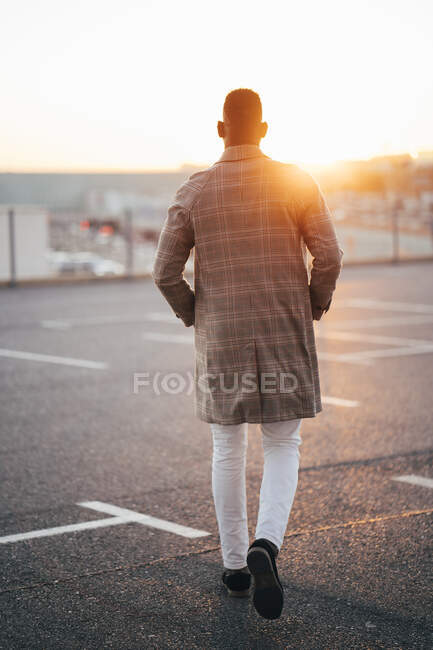 Hombre con las manos en los bolsillos caminando en el estacionamiento durante el atardecer - foto de stock
