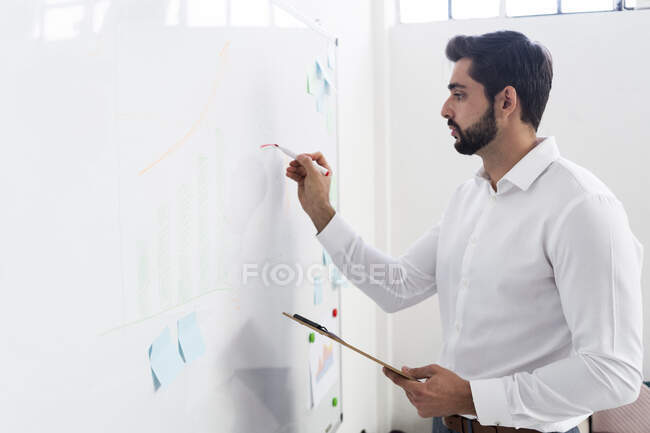 Empresário masculino desenho gráfico de negócios no quadro branco no local de trabalho — Fotografia de Stock
