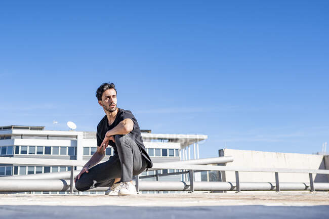Bell'uomo che distoglie lo sguardo mentre si accovaccia sul tetto durante la giornata di sole — Foto stock