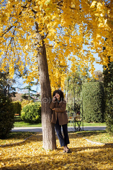 Жінка розмовляє по телефону, стоячи під деревом восени. — стокове фото