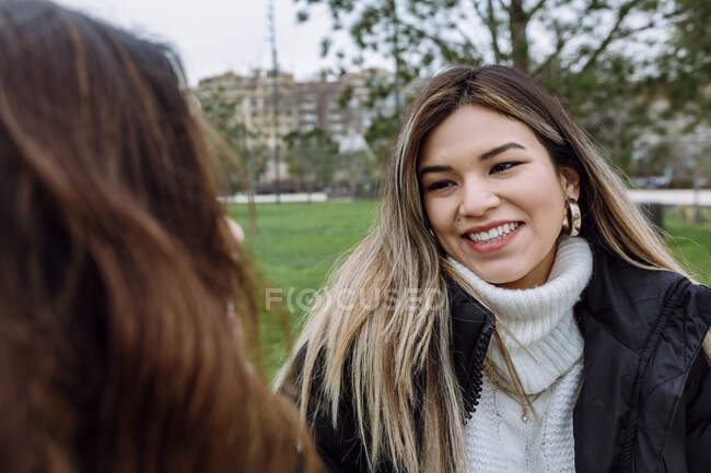 Mujer joven sonriente con amiga en el parque público - foto de stock