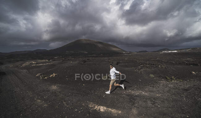 Happy male tourist dancing on volcano ash at El Cuervo Volcano, Lanzarote, España - foto de stock
