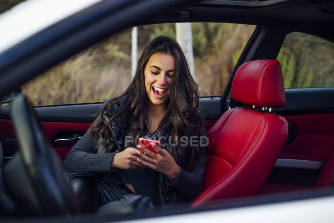 Захоплена жінка користується мобільним телефоном, сидячи в машині. — стокове фото