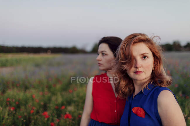 Femme adulte moyenne debout avec une amie dans un champ de pavot contre le ciel — Photo de stock