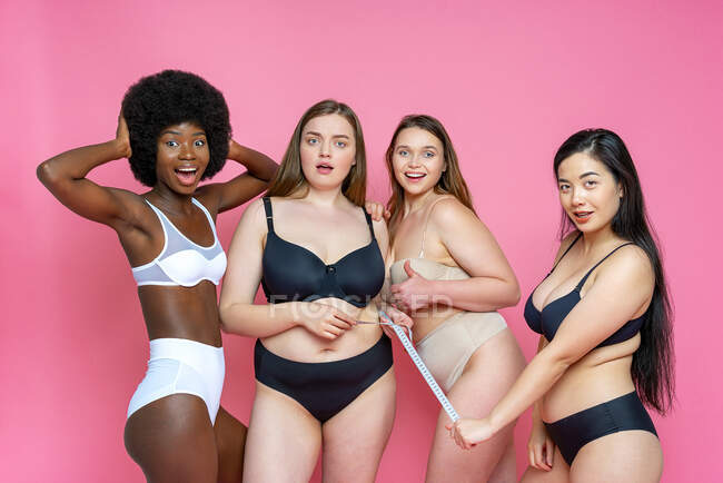 Sorpreso gruppo di multi-etnico modello femminile in lingerie con metro a nastro su sfondo rosa — Foto stock