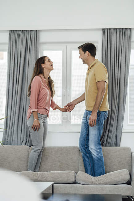 Allegro coppia matura che si tiene per mano mentre in piedi sul divano a casa — Foto stock