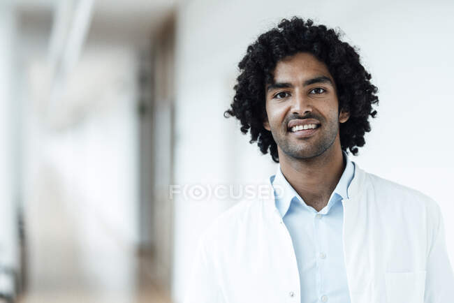 Посмішка молодого лікаря чоловічої статі з чорним кучерявим волоссям в коридорі лікарні. — стокове фото