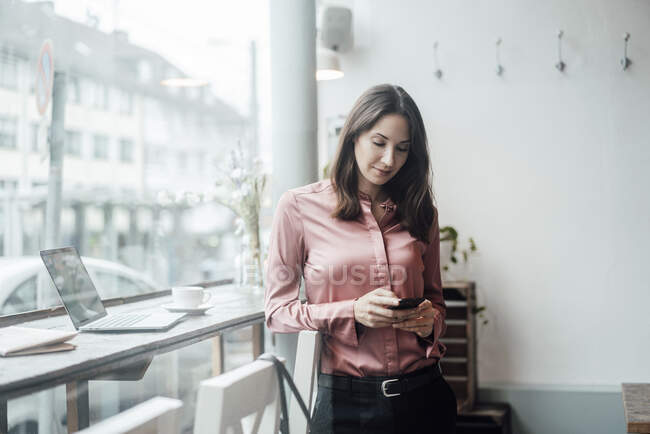 Жіночий підприємець пише повідомлення на смарт-телефоні в кафе. — стокове фото