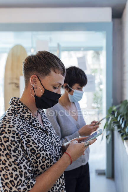 Jeune femme portant un masque protecteur à l'aide d'un téléphone portable alors qu'elle était au restaurant pendant la COVID-19 — Photo de stock
