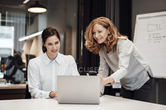 Feliz mujer de negocios discutiendo con una colega en la mesa de conferencias durante la reunión en la oficina - foto de stock