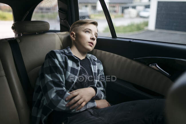 Nachdenklicher Junge schaut durchs Fenster, während er auf dem Rücksitz des Autos sitzt — Stockfoto