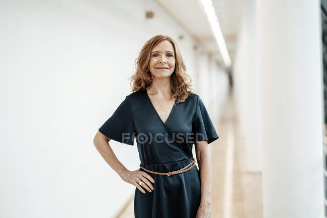 Smiling businesswoman with hand on hip in corridor at office — Stock Photo