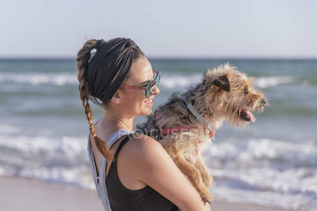 Mujer sosteniendo su perro en la playa - foto de stock