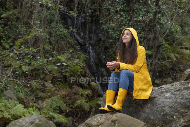 Nachdenklicher Wanderer im Regenmantel sitzt auf Felsen im Wald — Stockfoto
