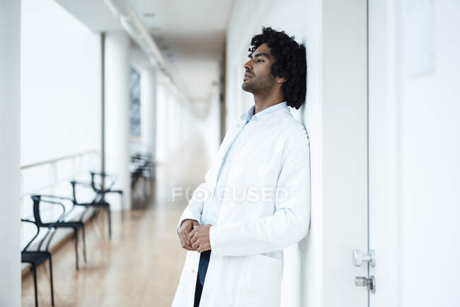 Thoughtful young male healthcare worker leaning on white wall at hospital corridor — Stock Photo