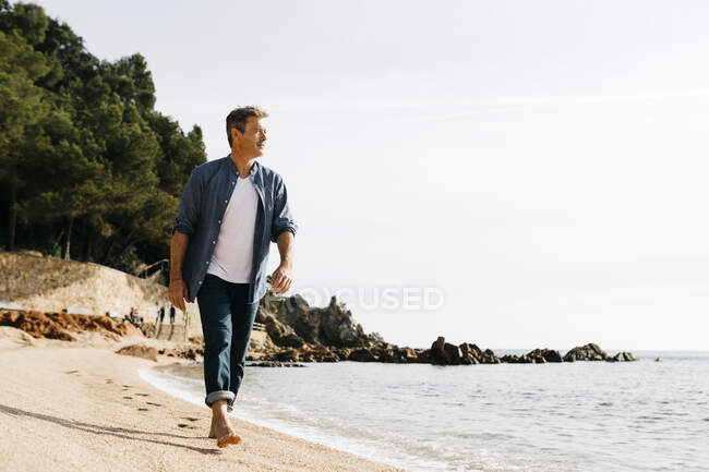 Uomo maturo che cammina sulla spiaggia contro il cielo limpido durante la giornata di sole — Foto stock