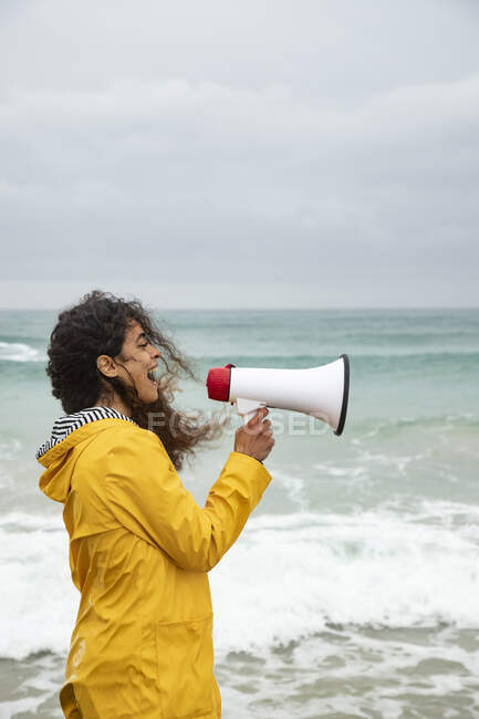 Woman screaming in megaphone while standing at beach — Stock Photo