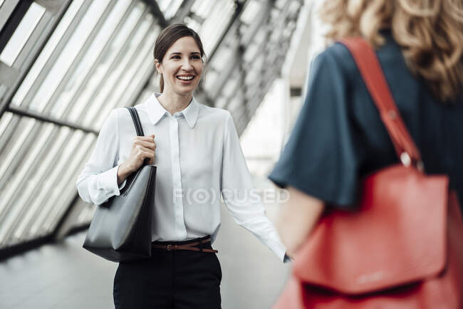 Улыбающаяся деловая женщина разговаривает с коллегами в офисном коридоре — стоковое фото