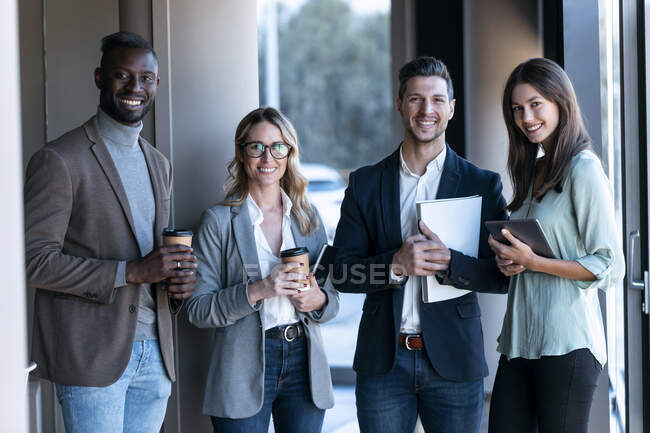 Equipo de negocios seguro sonriendo mientras están de pie juntos en la oficina - foto de stock