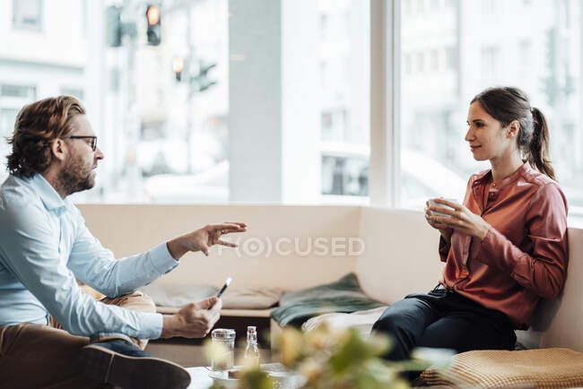 Женщина-предприниматель пьет кофе во время обсуждения с коллегой-мужчиной в кафе — стоковое фото