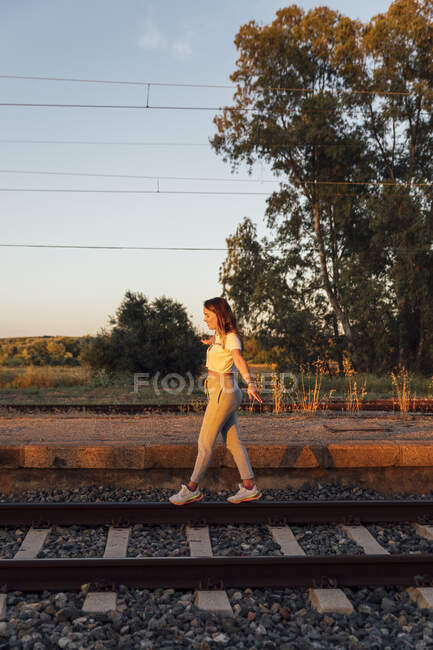 Mulher despreocupada com braços estendidos andando na via férrea contra o céu limpo — Fotografia de Stock