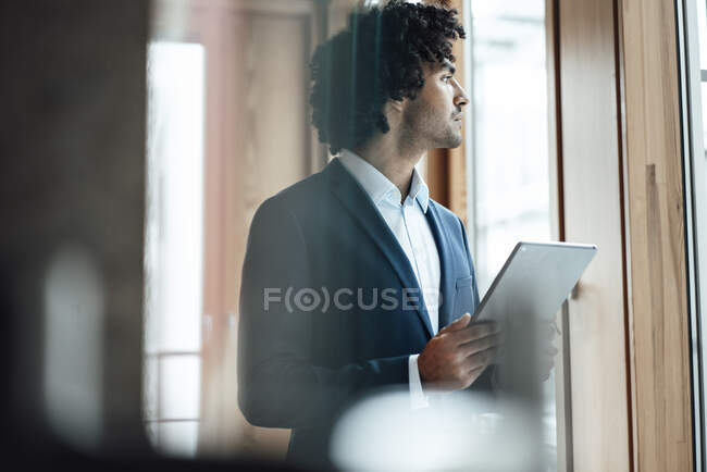 Thoughtful businessman looking away while holding digital tablet at office — Stock Photo