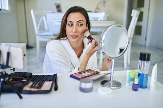 Influenciador feminino aplicando maquiagem enquanto vlogging no telefone inteligente em casa — Fotografia de Stock
