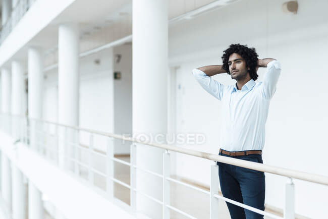 Молодий чоловік - підприємець, який тримає руки за головою, озираючись убік, роздумуючи в коридорі при офісі. — стокове фото