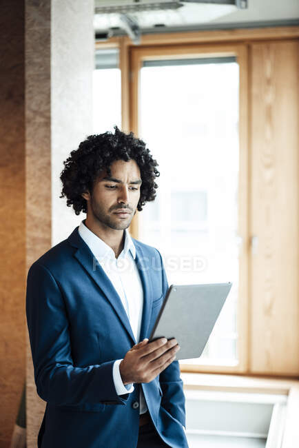 Fidato giovane professionista maschile con capelli neri ricci utilizzando tablet digitale in ufficio — Foto stock