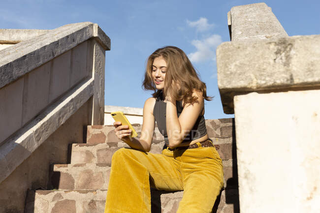 Young woman sitting in stone steps outdoors, looking at smart phone — Stock Photo