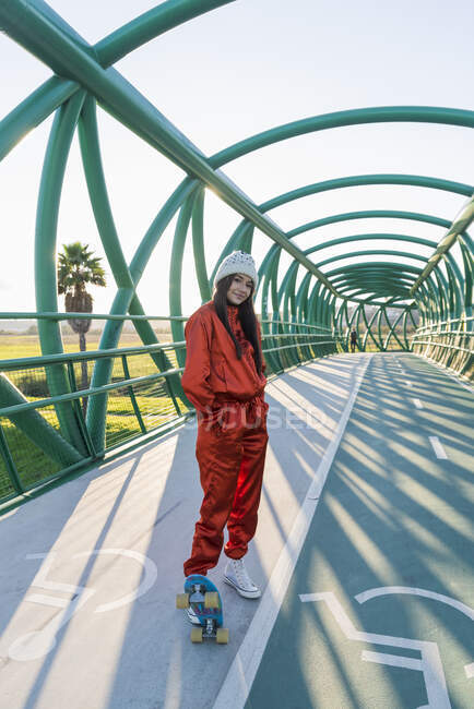Молода жінка з скейтбордом стоїть на мосту. — стокове фото