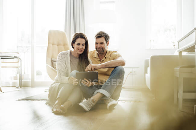 Sorrindo casal maduro usando tablet digital juntos enquanto sentado no chão em casa — Fotografia de Stock