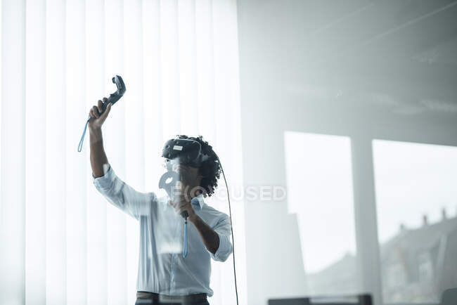 Young male professional wearing virtual reality headset playing with joystick in board room at office — Stock Photo