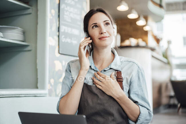 Female owner talking on smart phone while working in cafe — Stock Photo