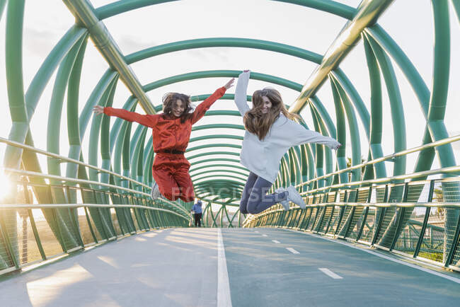 Amici spensierati con le braccia tese che saltano sul ponte — Foto stock